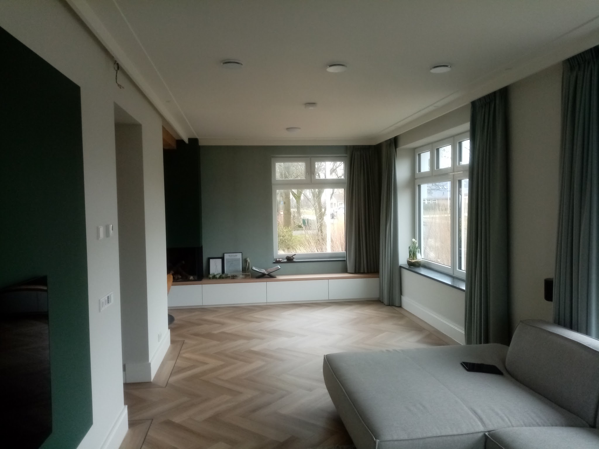 Ruime woonkamer met groene wanden, witte kozijnen en een visgraatvloer