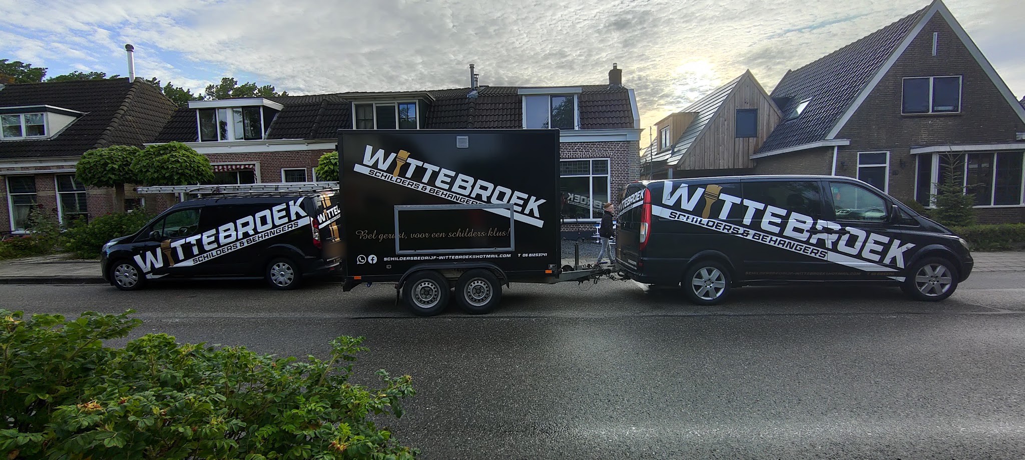 Twee zwarte bussen en een aanhanger van Wittebroek met de belettering Schilders & behangers